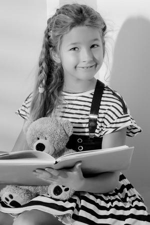 Little girl is reading a book to a teddy bear.の写真素材