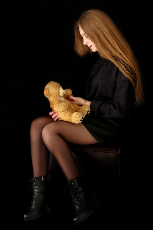 Teenage girl with a teddy bear on a black background.の写真素材