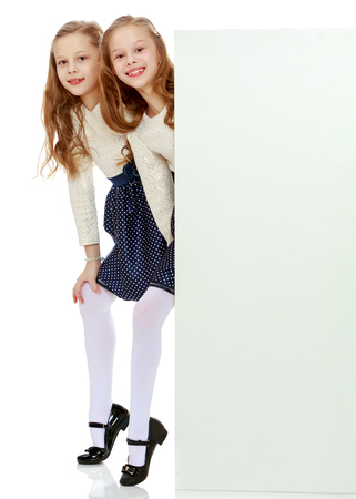 Two little girls peeking out from behind a white advertising banの写真素材