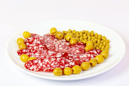 On the plate lies sliced sausage, green peas, and olives.の写真素材