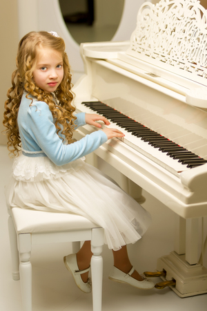 Beautiful little girl is playing on a white grand piano.の写真素材