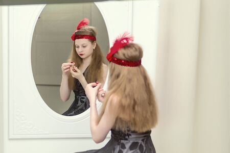 Beautiful girl of school age paints lips with lipstick and looks