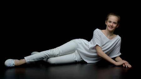 Cute little girl lying on the floor in the studio on a black bacの写真素材