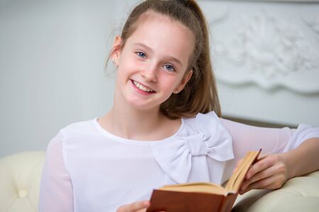 A little girl is sitting on the couch and reading a book.