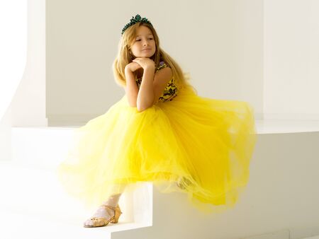 Cute little girl is sitting in the studio on the white stairs. sの写真素材