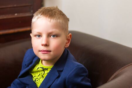 A cute little boy is sitting on a chair.