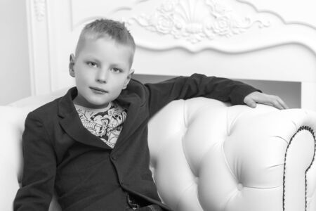 A little boy is sitting in the studio on a white sofa. The conceの写真素材