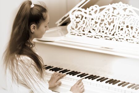 A teenage girl is playing on a white grand piano.の写真素材