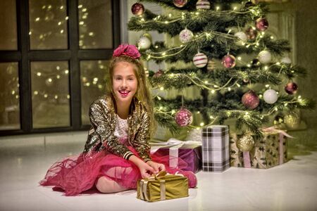 Pretty little girl smiling with present near the Christmas tree