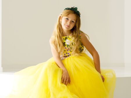 Cute little girl is sitting in the studio on the white stairs. style and fashion concept, happy childhood.の写真素材