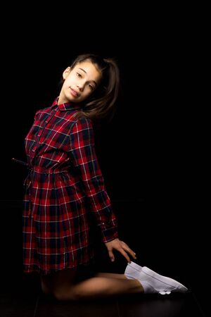 A little girl is kneeling on a black background in the studio.の写真素材