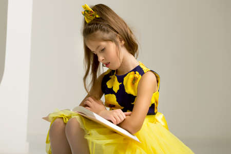 Beautiful little girl sitting on a white staircase and reading a book. The concept of children's...