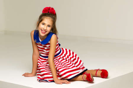 Cute little girl is sitting in the studio on the white floor.の写真素材