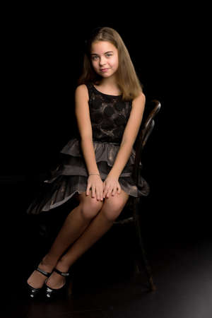 Portrait of a little girl sitting on an old Viennese chair, black background.の写真素材