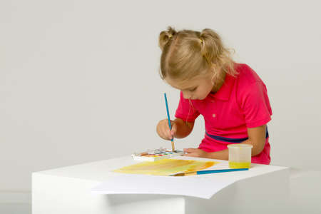 Beautiful Blonde Girl Standing at Table and Painting with Watercolorの写真素材