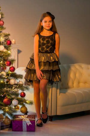 Girl in Stylish Dress Sitting on the Floor in Front of Christmas Tree.の写真素材