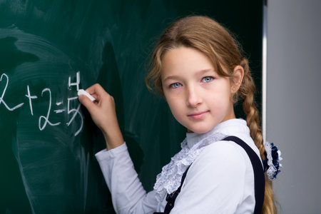 Schoolgirl writing on chalkboard in classroom