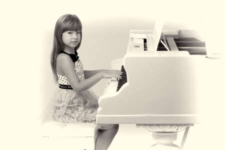 Lovely girl posing at white grand pianoの写真素材