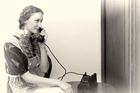 Pretty girl sitting and speaking via old phoneの写真素材