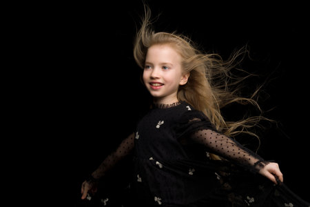 A beautiful little girl stands in the wind, her hair and clothesの写真素材