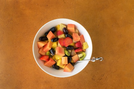 Fruit salad in white bowl on stone background. Camera top view