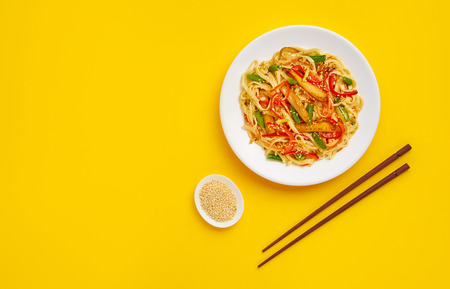 Udon noodles with fried chicken and vegetables on a yellow background. Flat lay with top view and...