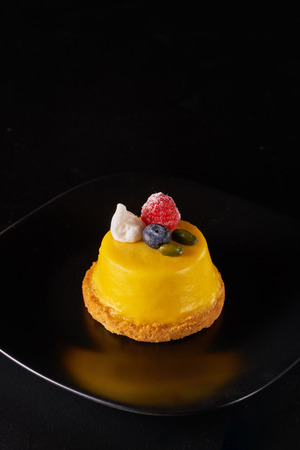 Mousse dessert covered with yellow glaze on black backgroundの写真素材