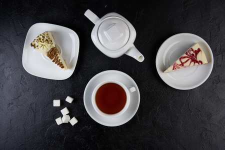 Two pieces of cheesecake, cup of tea and teapot on black background. Top view, Flat layの写真素材