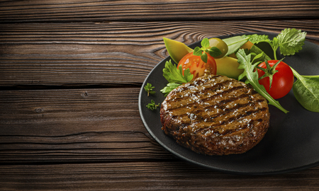Fried fresh large beef burger with salad and herbs on black plate on wooden tableの写真素材