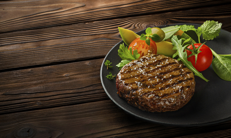 Juicy grilled burger cutlet with salad leaves on wooden tableの写真素材