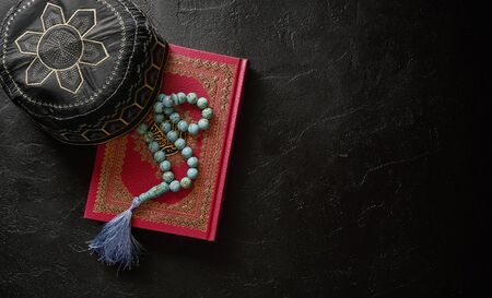 Koran with rosary and muslim hat on black stone or slate texture background. Islamic concept with copy spaceの写真素材