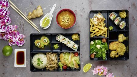 Japanese cuisine. lunch box set, sushi roll, salad, miso, chicken, sauce and wasabi on grey...