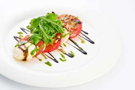 Mozarella cheese, tomatoes, arugula and pesto sauce in white plate.の写真素材