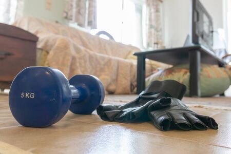 Concept quarantine home training set - 5 kg dumbbell and pair of gloves on floor near couchの写真素材