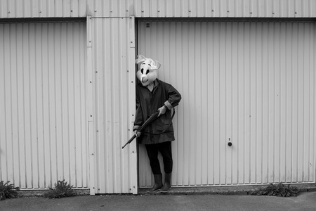 black and white photography. Woman wearing a rabbit mask hunting with shotgun in front of a garage doorの写真素材