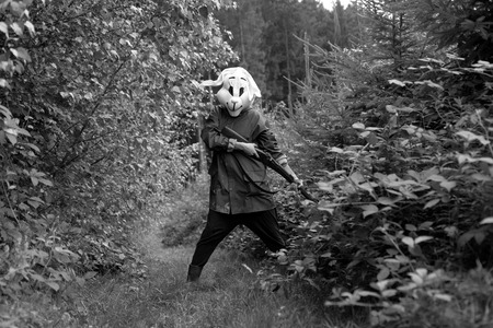 black and white photography. woman hunter wearing a rabbit mask hunting with shotgun in a forestの写真素材