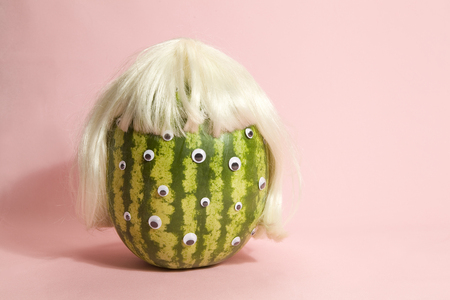 Freak watermelon wearing a wig and crown on a pink backgroundの写真素材