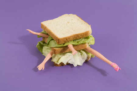 Parts of a doll's body in a sandwich with salad and soft bread on a minimal background color.
pop fun and quirky cannibalismの写真素材