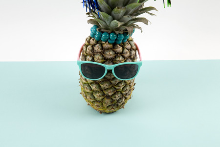 Playful pineapple wearing sunglasses and palm cocktail on a pop bi-color background turquoise and white like horizon. Minimal design still life photographyの写真素材