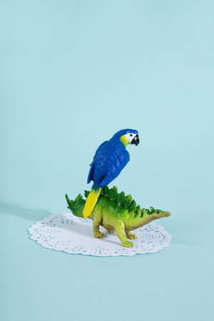 A dinosaur stegosaurus and a blue parrot on a white lace paper doily with a vibrant turquoise background.
Minimal offbeat still life photographyの写真素材
