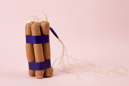 sticks of dynamite are replaced by industrial sausages. Photographic composition funny and offbeat on a vibrant pink studio background. Fun, minimal and surreal color still life photographyの写真素材