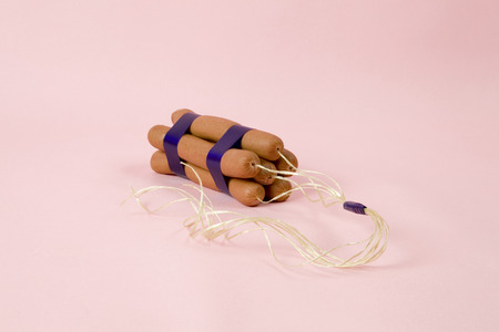sticks of dynamite are replaced by industrial sausages. Photographic composition funny and offbeat on a vibrant pink studio background. Fun, minimal and surreal color still life photographyの写真素材