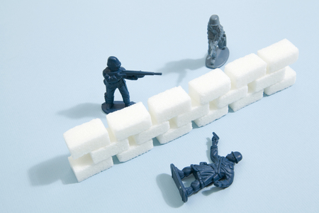 Battlefield with plastic soldiers separated by a wall border of white sugar cubes. Minimal color still life photographyの写真素材