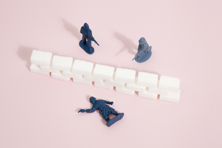 Battlefield with plastic soldiers separated by a wall border of white sugar cubes. Minimal color still life photographyの写真素材