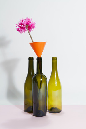 3 brown green glass bottles isolated on a bicolor background. a funnel with pink flower inside. Minimal wacky color still life photographyの写真素材