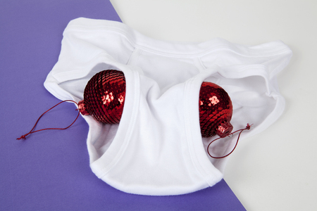 a red disco ball christmas decoration inside a y fronts underwear placed on a bicolor white and violet background. Minimal funny and quirky pop still life photographyの写真素材