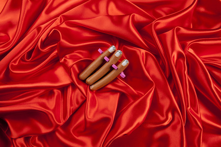 3 sausages with false nails placed in a manicure spacer like fingers on a vibrant red satin...