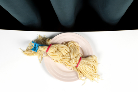 a delicious italian buttered spaghetti meal presented in a pink plate as blond braided hair. Minimal funny and quirky pop still life photography の写真素材
