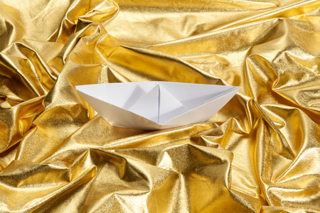 a paper origami boat sailing in a gold fabric choppy waters. Luxury composition. Minimal color still life photography.の写真素材