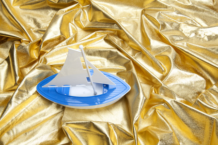 a plastic toy boat sailing in a gold fabric choppy waters. Luxury composition. Minimal color still life photography.の写真素材